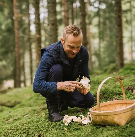 A man examining a mushroom beside a basket in woodland