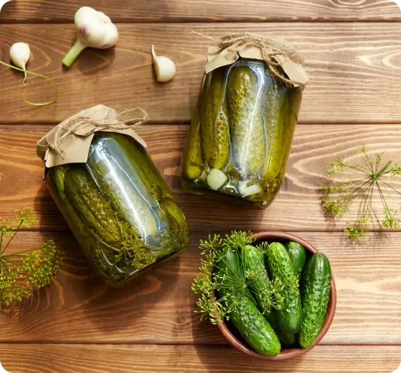 Jars of pickled cucumbers beside fresh cucumbers and garlic