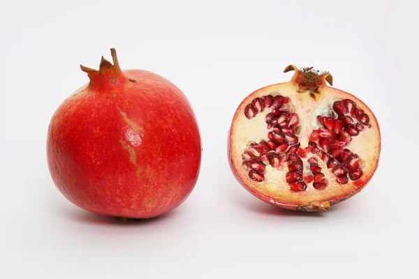 A whole red pomegranate and a cut half showing the red arils on a white background