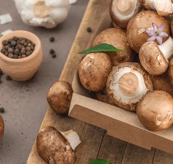 Brown mushrooms on a chopping board beside garlic and peppercorns