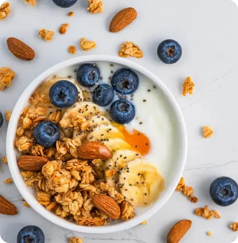 Bowl of yoghurt with granola, banana slices, blueberries and almonds