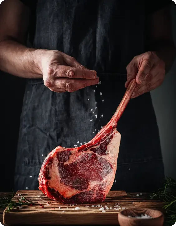 Cook seasoning a large bone-in steak on a chopping board