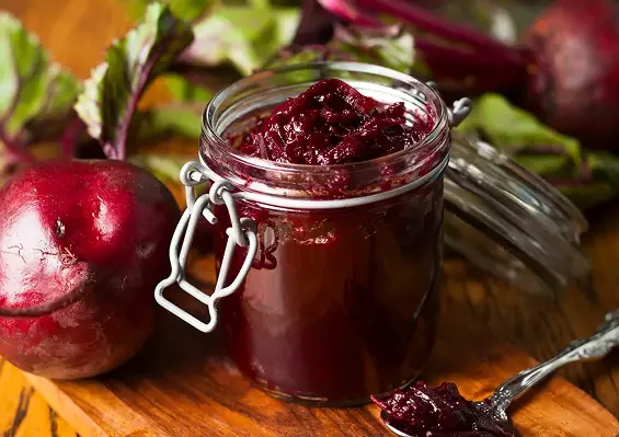 A jar of dark red beetroot preserve beside fresh beetroot