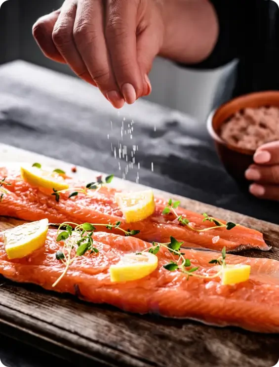 A hand sprinkling seasoning over salmon fillets with lemon slices