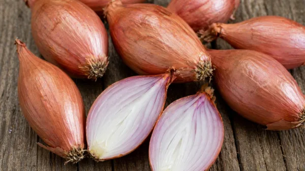Whole and halved elongated shallots on a wooden surface