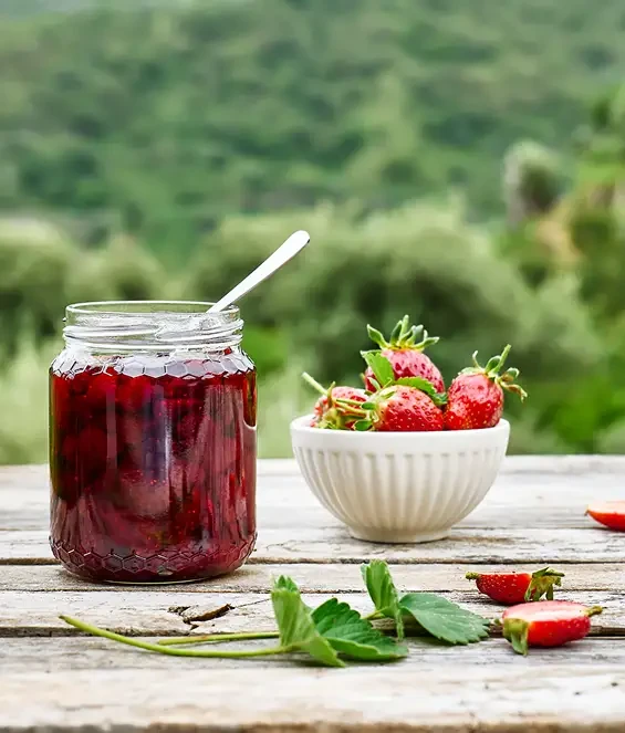 Jar of red jam beside fresh strawberries