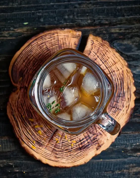 An amber drink with ice and herbs viewed from above