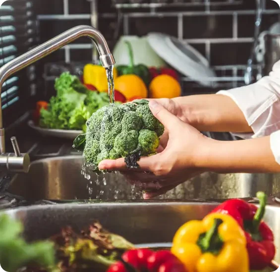 Hands washing broccoli under a kitchen tap
