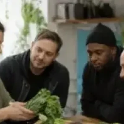 Group of diverse people gathered around a table examining fresh leafy vegetables together in a bright kitchen
